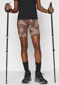 Shorts de sport marron avec un motif géométrique, accompagnés de bâtons de randonnée noirs et de chaussures assorties. Des chaussettes noires classiques complètent le look.