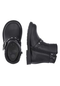 Botas de tobillo de cuero negro con cremallera lateral, detalles metálicos y un panel texturizado en el talón. Suela plana de goma con un patrón de agarre circular.