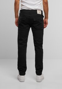 Jeans negri din denim, cu croi slim, având două buzunare în spate și un etichetă pe talie. Purtați cu adidași albi.