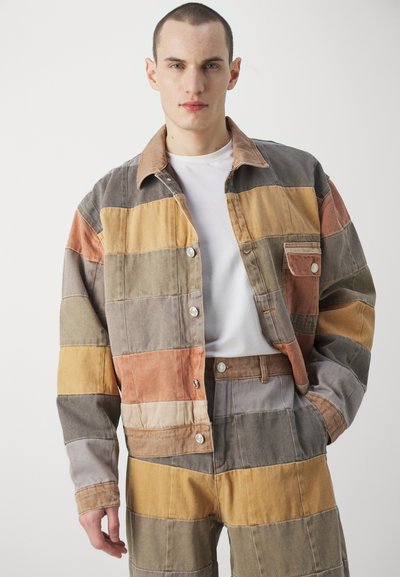 Patchwork-Jeansjacke mit orangefarbenen, gelben, grauen und braunen Streifen. Verfügt über eine knöpfbare Front, klassischen Kragen und eine Brusttasche.