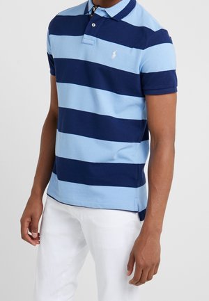Polo à rayures alternées bleu clair et bleu foncé, avec un col à deux boutons, des manches courtes, et un petit logo brodé sur la poitrine.