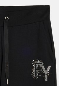 Un pantalon de survêtement noir présente une large ceinture élastique avec un cordon de serrage, ornée de strass formant les lettres "FY" d'un côté.