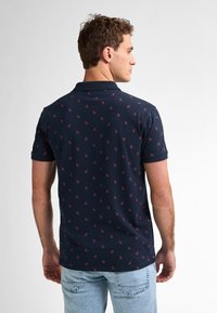 Polo de color marino con pequeño patrón floral rojo, de manga corta y con cuello. El material parece suave y ligero, adecuado para un uso casual.