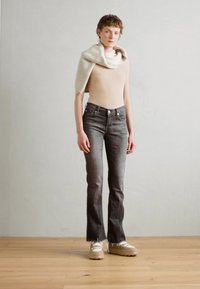 Top sans manches beige, jeans gris évasés et écharpe en tricot crème. Un tissu texturé et des chaussures décontractées complètent la tenue sur un fond neutre.