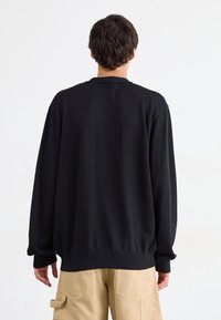 Schwarzer Rundhalsausschnitt-Pullover mit langen Ärmeln, gerippten Bündchen und Saum, aus weichem Stoff. Über beigen Cargohosen getragen.