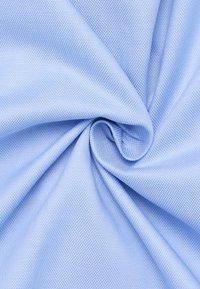 Lichtblauwe textuurstof, geweven in een fijn patroon, hangt om zijn soepelheid en zachtheid te tonen. Ideaal voor kleding en meubels.