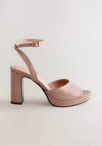 Nude korkokengät, joissa on kiiltävä pinta, paksu korko, alustapohja, avoin varvas ja nilkkaremmi kultaisella soljella.