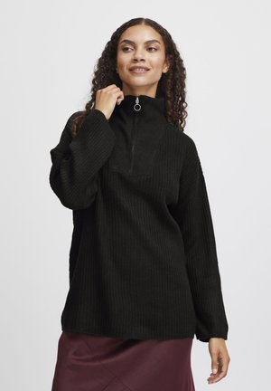 Zwarte geribbelde pullover trui met een hoge hals, voor half-ritsluiting en lange mouwen, gecombineerd met een bordeauxrode rok.