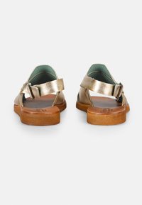 Sandales en cuir métallisé doré avec une sangle à boucle, dos ouvert et semelles texturées brunes. Doublées avec un matériau de couleur bleu-vert pour le confort.