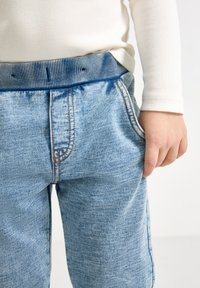 Lyseblå jeansbukser med en teksturert overflate, med stripete midjebånd, synlige sømmer og sidelommer.