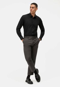 Chemise noire à manches longues avec boutons, associée à un pantalon slim gris foncé et des chaussures noires chunky. Tissu lisse et coupe ajustée.