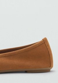 Chaussure plate en suede marron avec un bout arrondi, une semelle plate et des coutures lisses le long du bord. Design minimaliste sans matériel ou motifs visibles.