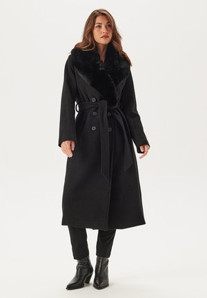 Sort trenchcoat med krave af kunstpels, dobbeltradet design og aftageligt bælte. Lavet af et struktureret stof med lange ærmer.