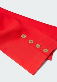 Poignet de chemise rouge vif avec quatre petits boutons dorés alignés en rang sur fond blanc propre.