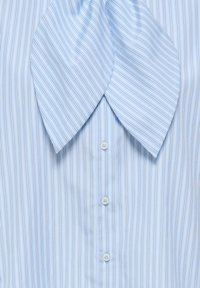 Chemise bleu clair à fines rayures verticales avec un grand col à nœud papillon proéminent, dotée de boutons blancs au centre.