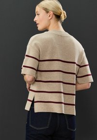 Beige striktrøje med korte �ærmer og vinkler i burgunder. Bunden har sideskår for en afslappet pasform. Båret med mørke denimjeans.