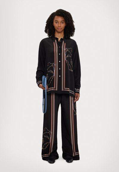 Black blouse with colorful embroidered designs and vertical stripes, paired with matching wide-leg trousers and a blue strap bag.