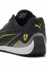 Schwarzer Ledersneaker mit gelben Akzenten, perforiertem Design und Puma-Logo. Verfügt über ein Ferrari-Schild-Emblem und eine weiße Gummisohle.