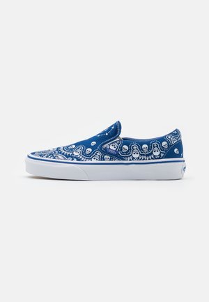 Baskets bleu sans lacets avec motif de crâne blanc et motif cachemire, semelle en caoutchouc blanche, et étiquette du logo Vans sur le côté.