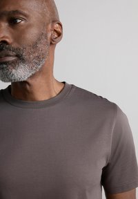 Camiseta de manga corta y cuello redondo en un tono marrón apagado. Fabricada con una tela suave y con una textura sutil. Diseño simple, sin logotipos visibles.