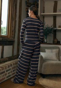 Compleu de loungewear cu dungi bleumarin și crem, format dintr-un top cu mânecă lungă și pantaloni cu pantaloni largi, realizat dintr-un material moale, cu o croială relaxată.