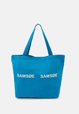 Blå kanvas tote-bag med to hvite SAMSØE-logoer. Har lange, robuste håndtak og et enkelt design, egnet for daglig bruk.