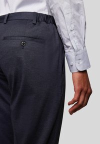 Donkerblauwe, textuurachtige broek met een elastische tailleband, voorzien van een achterzak met knoopsluiting en een subtiele patroon op de mouw van het shirt.