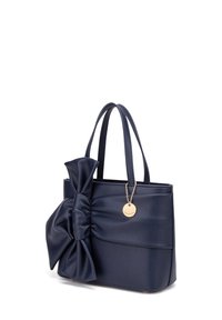 Marineblauwe leren tote bag met een opvallende strikdetail aan één kant, een gladde textuur, dubbele handvatten en een gouden hanger eraan bevestigd.