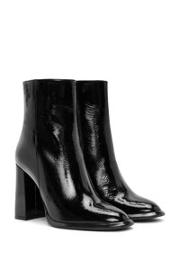 Bottines en cuir verni noir avec un bout carré, un talon bloc haut, une texture lisse et un minimum de détails de couture.
