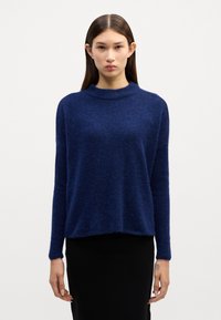 Strickpullover in Marineblau mit hohem Kragen, langen Ärmeln und lockerer Passform. Weiche Textur und leicht unregelmäßiger Saum für zusätzliche Details.