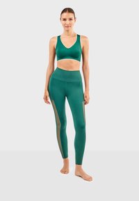 Groene sportbeha en legging set van rekbaar materiaal. Leggings hebben mesh panelen aan de zijkanten. Soepele textuur met een slim fit ontwerp.
