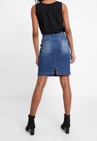 Denimová sukně v tmavě modré barvě s přiléhavým střihem, detailem rozparku na zadní části a dvěma zadními kapsami. V kombinaci s černými kotníkovými botami.