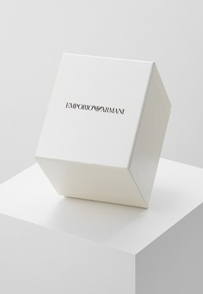 Caja triangular blanca con acabado mate, que presenta el logo de "Emporio Armani" en negro en la parte frontal. Textura suave, diseño minimalista.