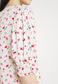 Blusa in tessuto leggero caratterizzata da una stampa floreale in tonalità rosse e rosa, con maniche a sbuffo arricciate e una finitura morbida e texturizzata.