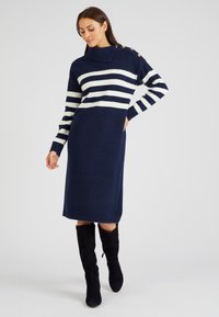 Abito maglia navy con righe orizzontali bianche, caratterizzato da un colletto alto e dettagli in bottone sulle spalle. Scollo aderente e lunghezza media.