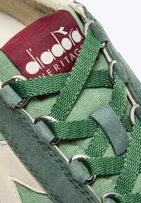 Sneaker verde con tomaia testurizzata, accenti in suede, occhielli in metallo e un'etichetta logo bordeaux sulla linguetta. I lacci sono intrecciati e spessi.