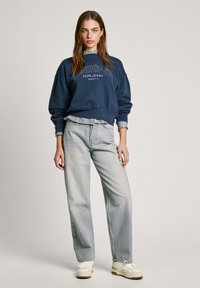 Mörkblå sweatshirt med texten "LONDON", kombinerad med ljusgrå raka jeans. Vita sneakers fulländar den avslappnade klädstilen.