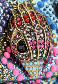 Decorative brooch featuring gold-tone metal with multi-colored rhinestones. The design is intricate, resembling an ornate hand shape.