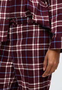 Πυζάμα σε μπορντό καρό σχέδιο με λευκές και μπλε γραμμές, φτιαγμένη �από μαλακό ύφασμα με ελαστική μέση και ρυθμιζόμενο κορδόνι.