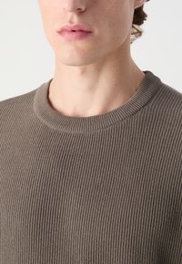 Suéter marrón acanalado con cuello redondo, que presenta una superficie texturizada y un ajuste ceñido, destacando la suavidad y elasticidad de la tela.