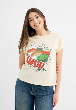 Camiseta color beige claro con un gráfico colorido de sushi y el texto "Amante del Sushi". Mangas cortas con un ajuste relajado y una textura suave.