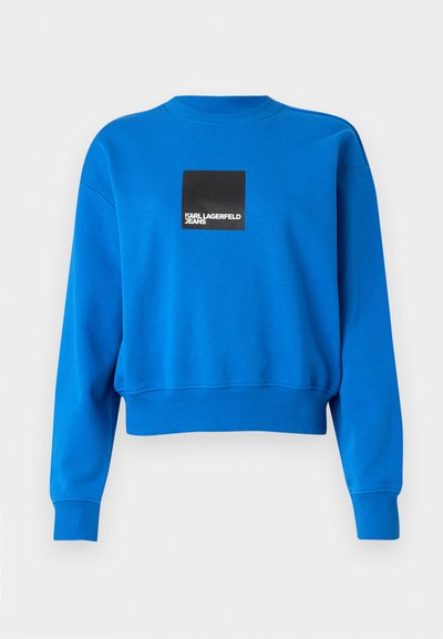 Sweatshirt bleu raccourci en tissu doux, avec un logo carré noir et un texte blanc, des poignets et un col côtelés.