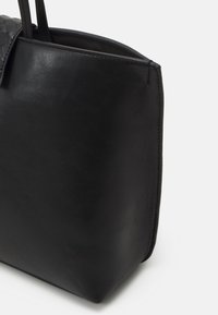 Borsa a tote in pelle nera con texture liscia e forma strutturata, dotata di due manici e design minimalista.