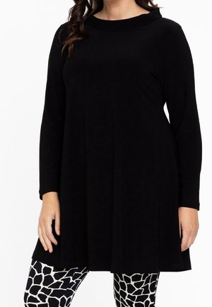 Tunika nera a maniche lunghe con scollatura rotonda, realizzata in tessuto morbido, abbinata a leggings bianchi e neri con un motivo a giraffa.