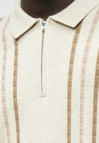 Μπεζ πόλο μπλούζα με φερμουάρ στον γιακά, που διαθέτει κατακόρυφες ρίγες σε ανοιχτό καφέ και υφαντή σχέδιο.