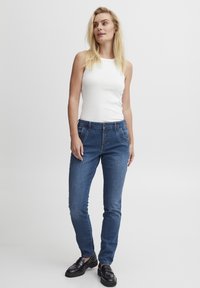 Sinine denimi teksad viie nööbi sulgemisega, kitsas lõige ja eesmine taskud. Koos valge ilma varrukateta topsi ja mustade mokassiinidega.