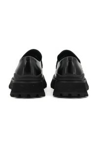 Zwarte leren schoenen met een dikke rubberen zool, voorzien van een brede hak, een gestructureerde afwerking en een minimalistisch ontwerp. Achteraanzicht weergegeven.