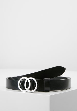 Czarny skórzany pasek z srebrną klamrą podwójnego pierścienia, zwinięty i leżący na białej powierzchni na tle jasnego, jednolitego tła.