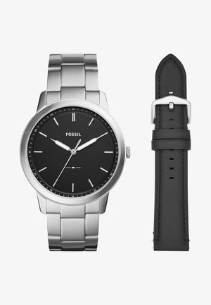 Montre-bracelet Fossil en acier inoxydable avec cadran noir, aiguilles et index argentés, présentée avec un bracelet en cuir noir supplémentaire.