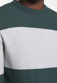 Pull rayé vert et gris avec un tricot texturé, un col rond et des blocs de couleur horizontaux distincts dans un tissu doux.